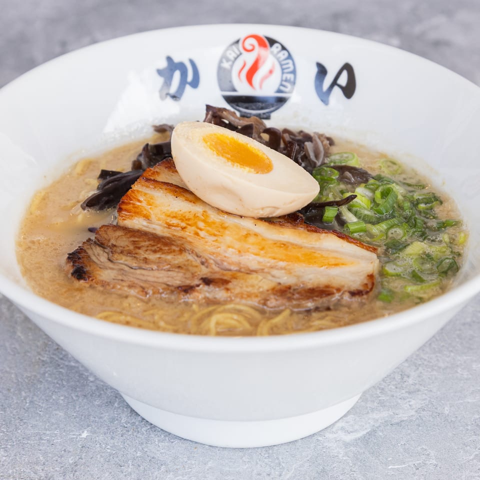 A bowl of Kai Ramen with pork belly, a soft-boiled egg, green onions, and mushrooms.