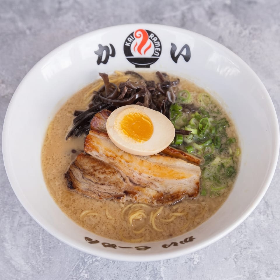 Kai Ramen bowl with pork belly, soft-boiled egg, green onions, and mushrooms in a rich broth.
