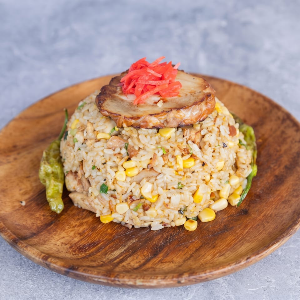Fried rice with corn, pork belly, and red pickled ginger, served on a wooden plate.