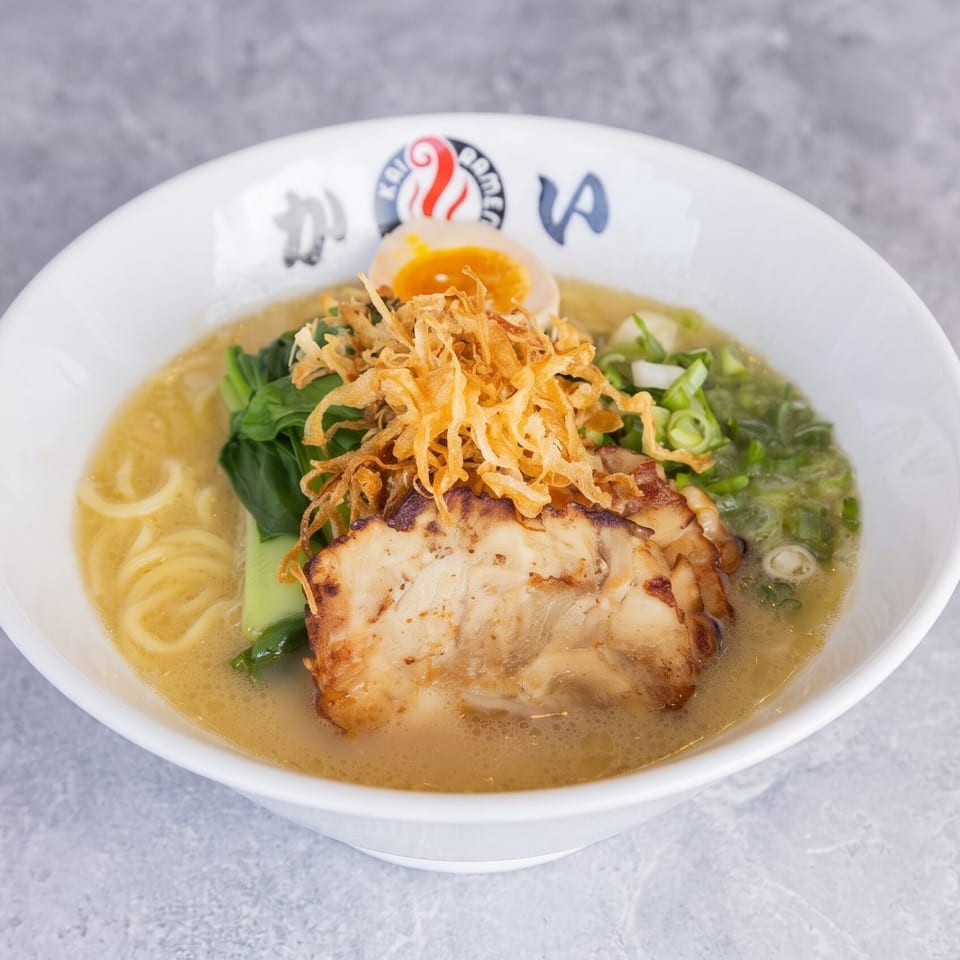 A bowl of Kai Ramen with pork, bok choy, egg, scallions, and crispy fried onions.